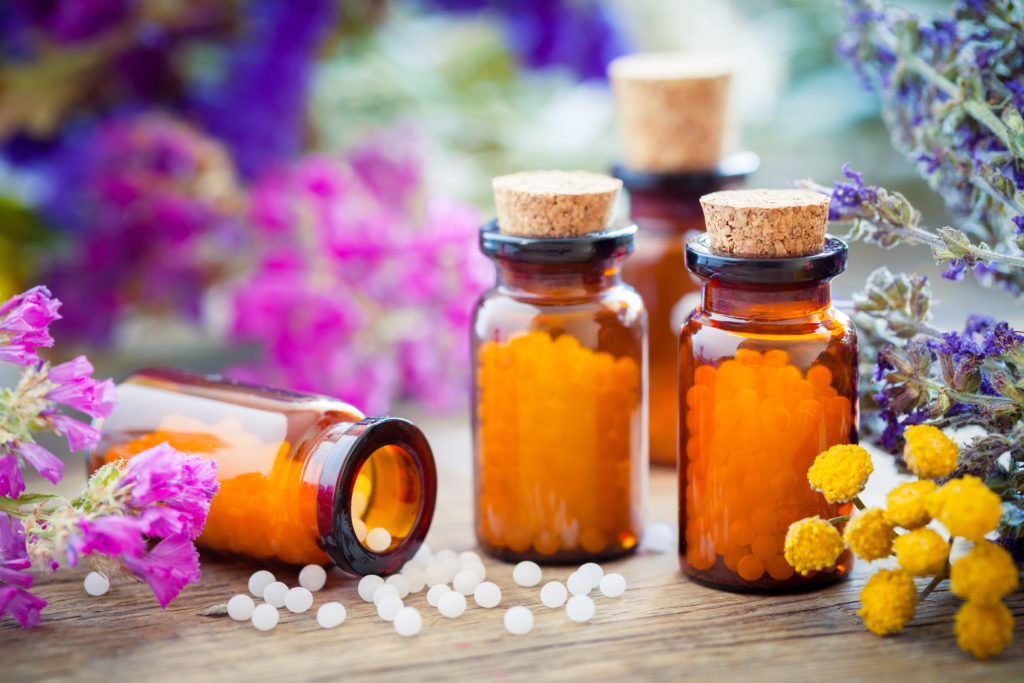Homöopathische Arzneifläschchen mit Globuli und Blüten